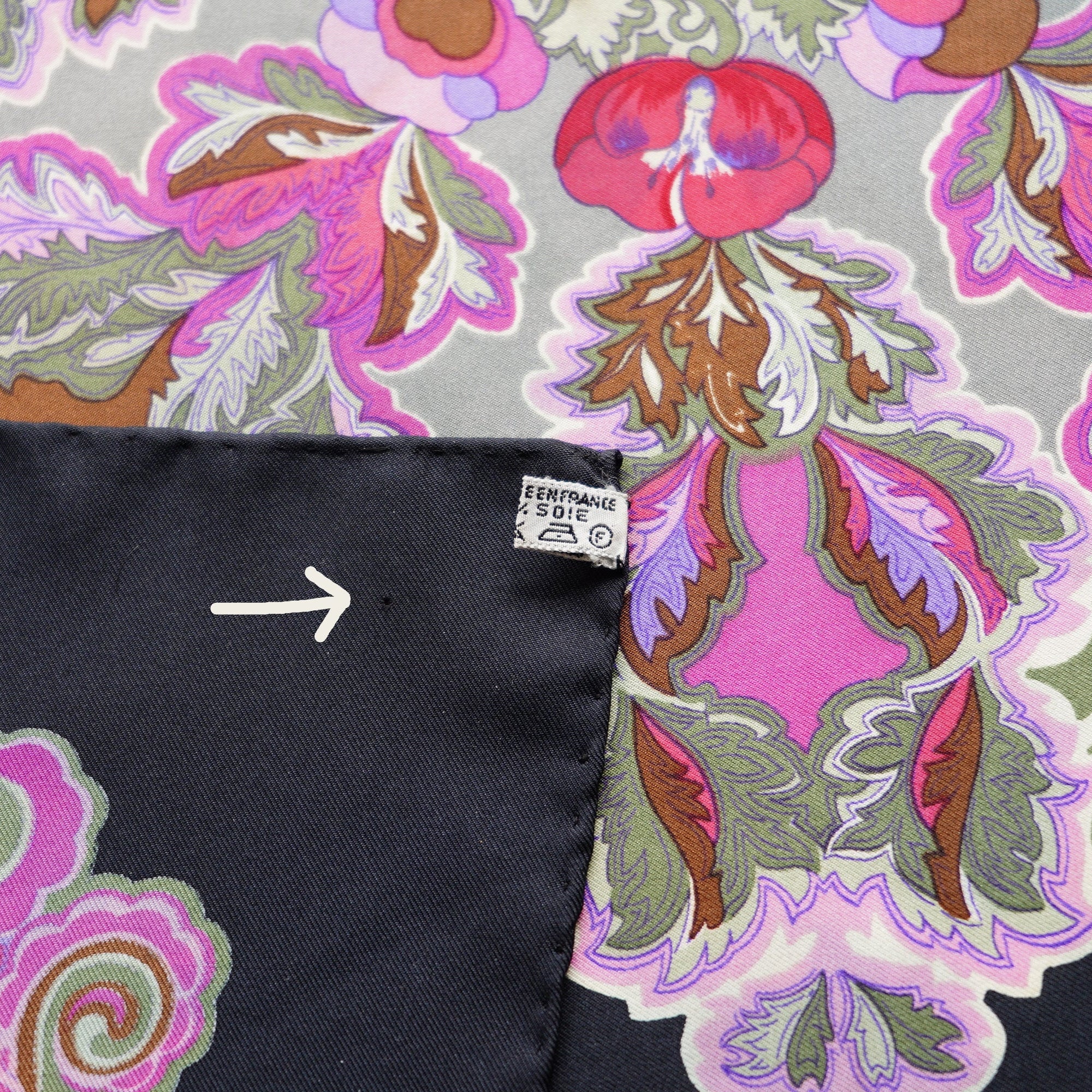 Gros plan sur un coin du foulard "Anémones", une flèche montre un second micro-trou sur le tissu.