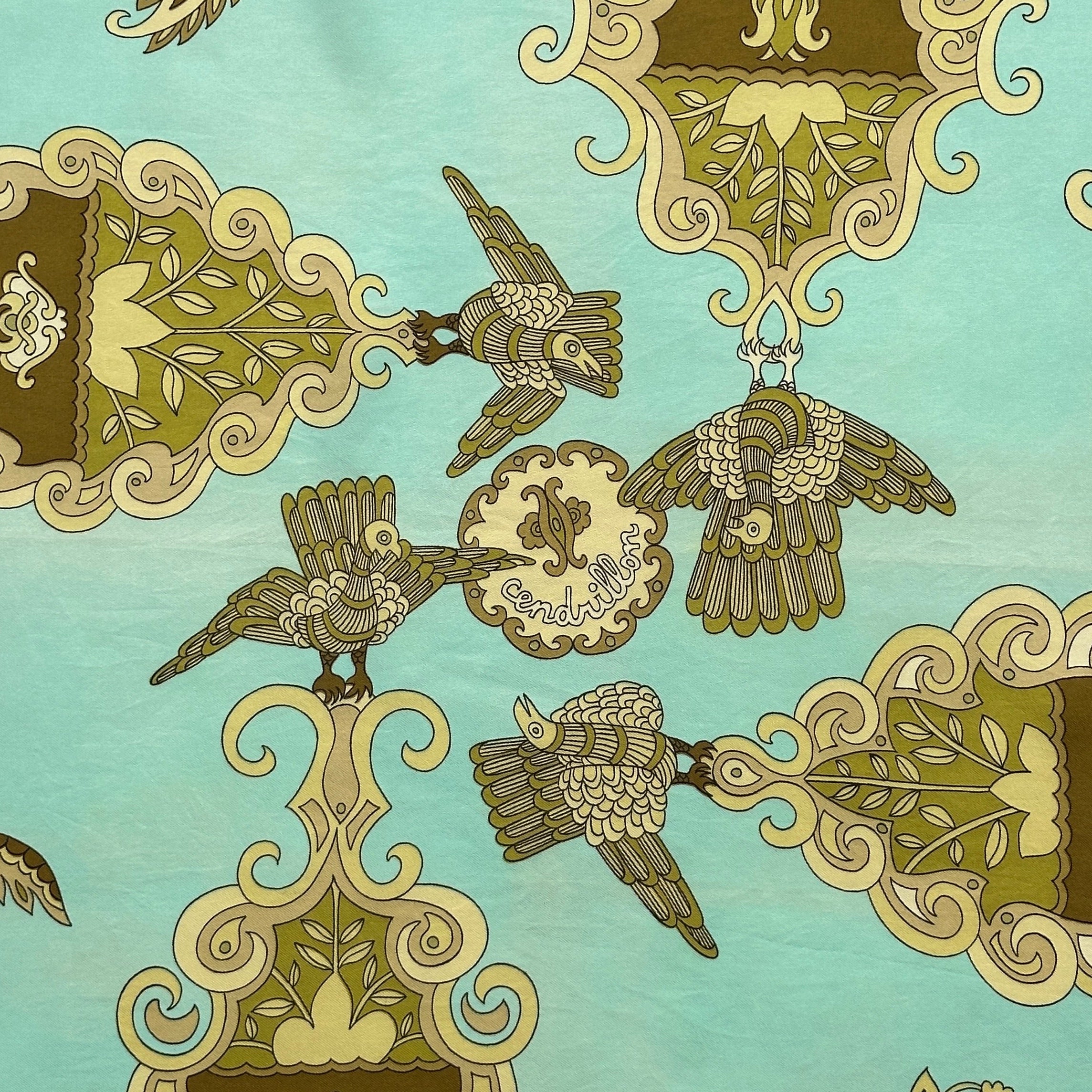 Gros plan sur le centre du foulard : oiseaux stylisés tenant un médaillon inscrit "Cendrillon" sur fond vert pâle.